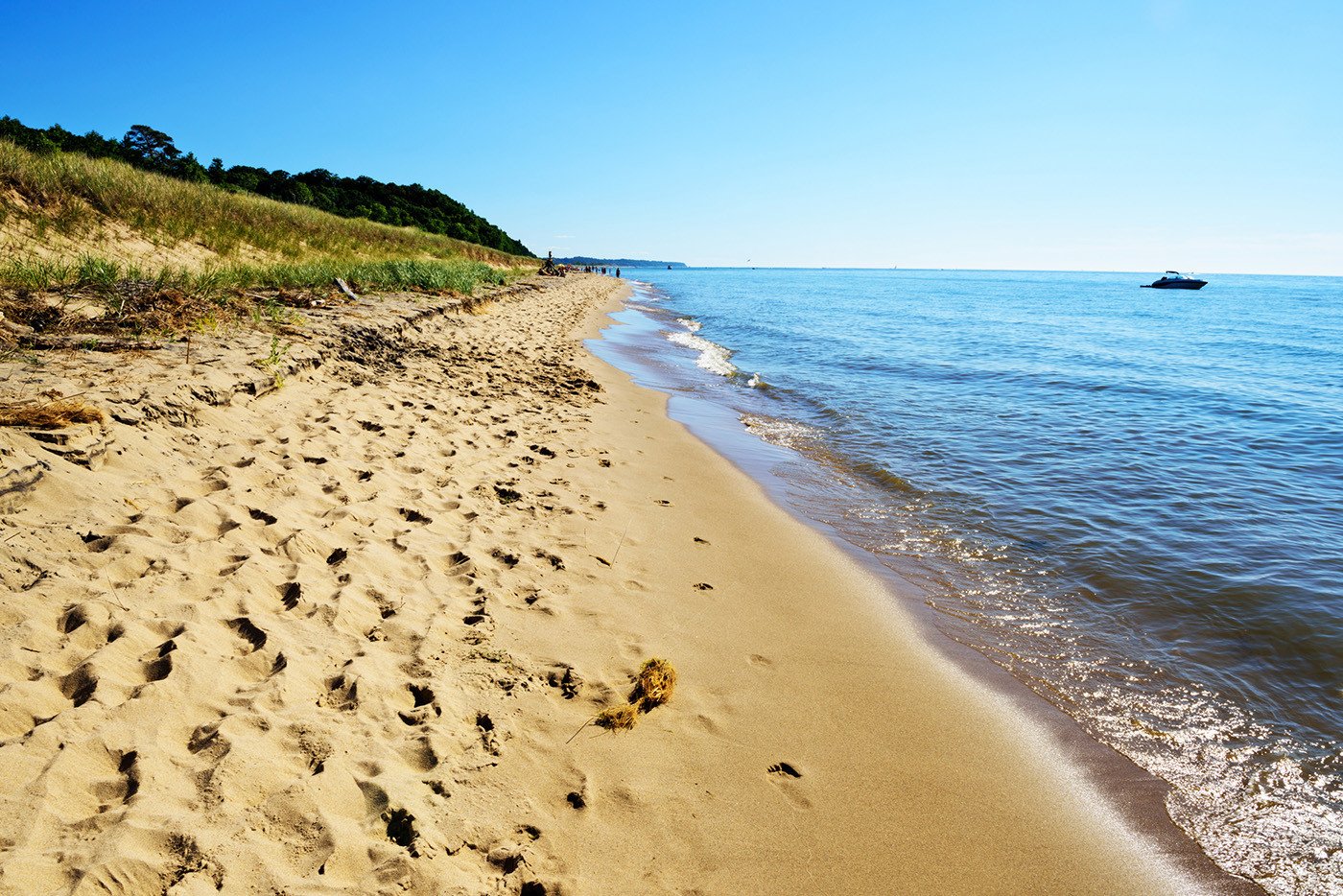 Sandy shore of Lake Michigan at Saugatuck Dunes State Park in Allegan County, Michigan. Distant people and moored boat.